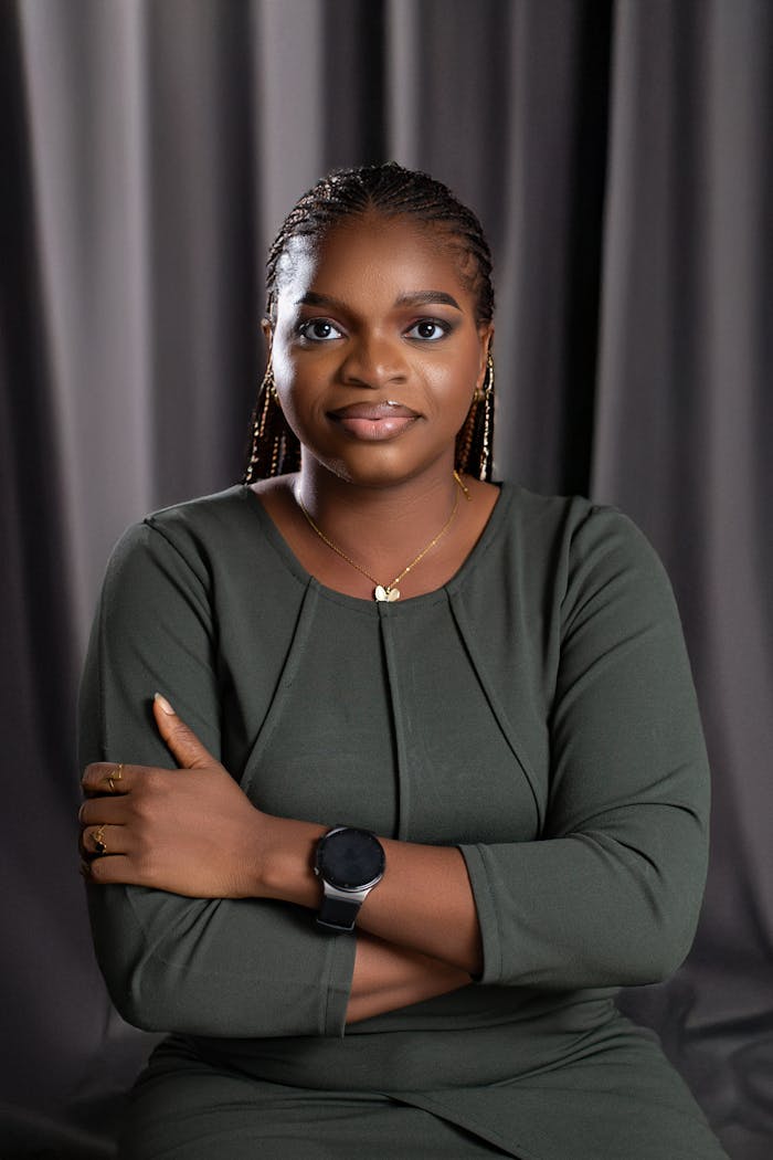 who-we-are Portrait of a confident African woman in a green dress, seated with arms crossed.