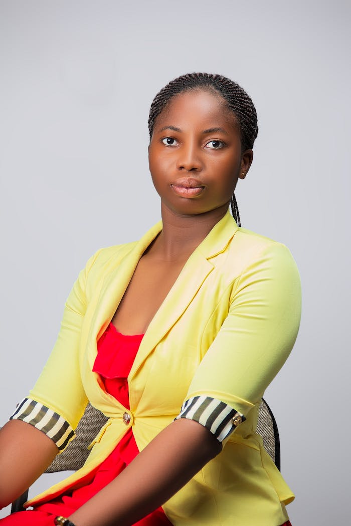 Professional woman poses confidently in a yellow blazer, neutral backdrop.