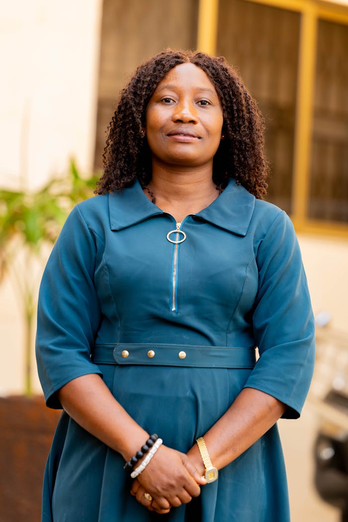 Confident woman standing outdoors in a blue dress, looking directly at the camera.