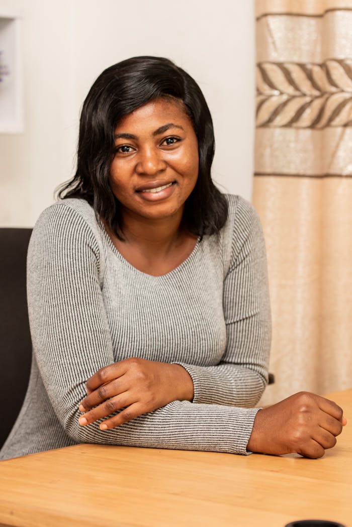 A cheerful black woman with a warm smile sitting at a table in a cozy indoor setting.